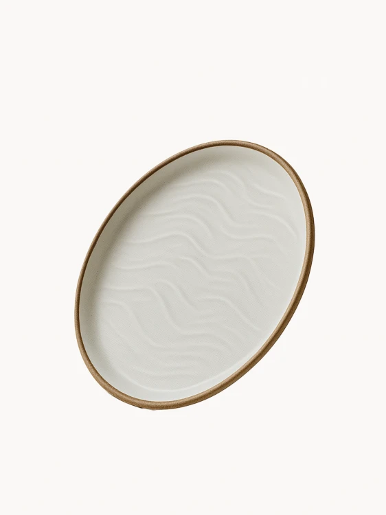 An oval ceramic platter in a matte off-white finish features a textured, wavy sand dune pattern on its interior and a natural brown rim.