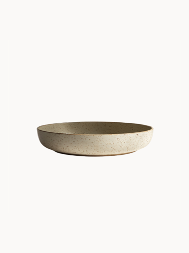 A shallow, round ceramic bowl with a speckled beige and light grey texture, on a plain white background.