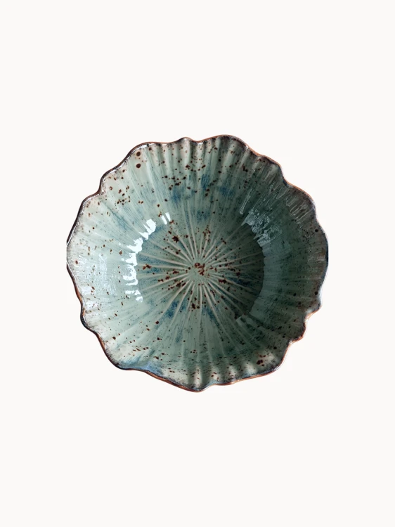 A top-down view on a rustic ceramic bowl with a mottled light blue and beige glaze with brown speckled details, on a plain white background.