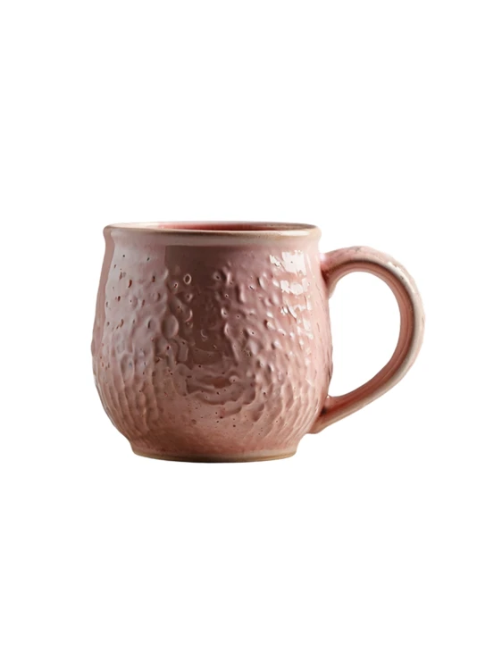 A pink ceramic mug with a bulbous shape and a rounded handle on a plain white background. The body features a highly textured, dimpled surface resembling craters, finished with a glossy glaze.
